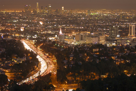 View of the illuminated Los Angeles skyline at night with glowing traffic light trails on the highway and dense urban sprawl Los Angeles California United States. View of the illuminated Los Angeles skyline at night with glowing traffic light trails on the highway and dense urban sprawl Los Angeles California United States.