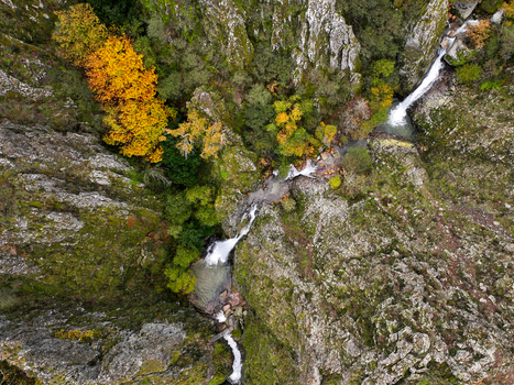 Aerial view of Poco do Inferno waterfall cascading down rocky cliffs surrounded by vibrant autumn foliage in Manteigas Guarda District Portugal. Aerial view of Poco do Inferno waterfall cascading down rocky cliffs surrounded by vibrant autumn foliage in Manteigas Guarda District Portugal.