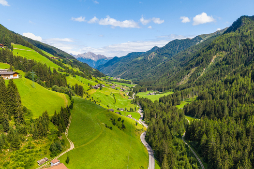 Aerial view of the lush green valley of Muhlwald with dense pine forests rolling alpine meadows a winding road and traditional houses in Muhlwald Trentino Alto Adige Italy. Aerial view of the lush green valley of Muhlwald with dense pine forests rolling alpine meadows a winding road and traditional houses in Muhlwald Trentino Alto Adige Italy.