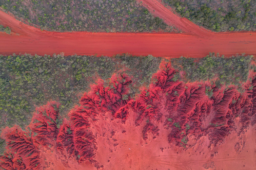 Aerial view of a vibrant red dirt road cutting through eroded terrain and sparse bushland in Broome Western Australia Australia.