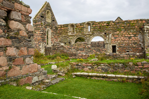View of the ancient stone ruins of Iona Nunnery with pink granite walls and Romanesque arches under an overcast sky in Baile Mor Scotland United Kingdom. View of the ancient stone ruins of Iona Nunnery with pink granite walls and Romanesque arches under an overcast sky in Baile Mor Scotland United Kingdom.
