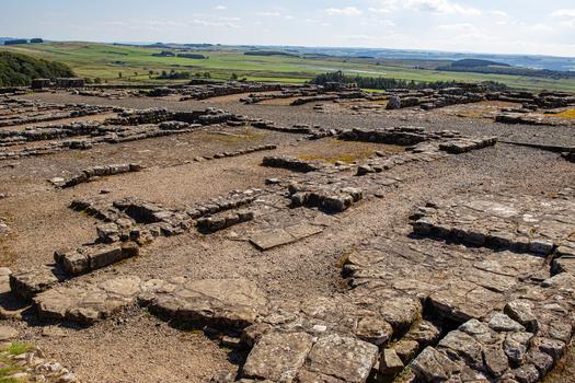 View of the ancient stone foundations of Vindolanda Roman fort overlooking the rolling green hills of the English countryside Hexham England United Kingdom. View of the ancient stone foundations of Vindolanda Roman fort overlooking the rolling green hills of the English countryside Hexham England United Kingdom.