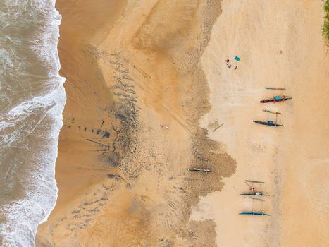 Aerial view of traditional outrigger boats resting on a sandy beach with crashing ocean waves and people Galle Southern Province Sri Lanka.