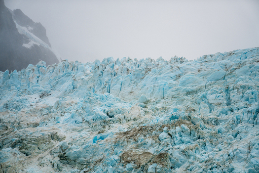 View of the Drygalski Fjord glacier with jagged blue ice formations deep crevasses and snow capped mountains under an overcast sky in South Georgia and the South Sandwich Islands.