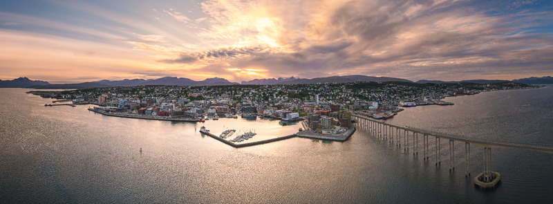 Aerial view of the city of Tromso with its iconic bridge harbor and surrounding mountains illuminated by the soft golden light of a late summer sunset in Tromso Troms Norway.