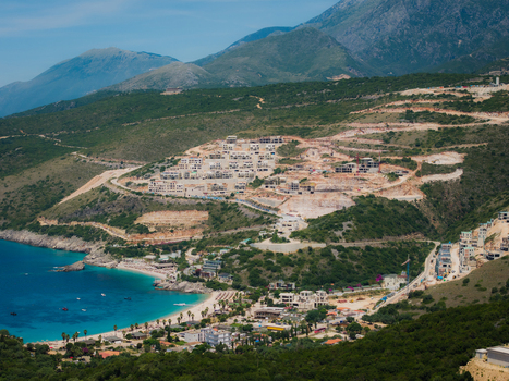 Aerial view of Aquarium Beach and the turquoise bay with construction sites on the hillside and green mountains in Jala Vlore County Albania. Aerial view of Aquarium Beach and the turquoise bay with construction sites on the hillside and green mountains in Jala Vlore County Albania.