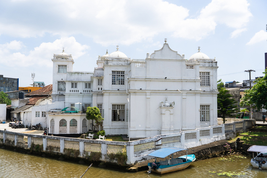 View of the historic white Muhideen Jumma Mosque with its domes and architecture along the waterfront with small boats Matara Southern Province Sri Lanka.