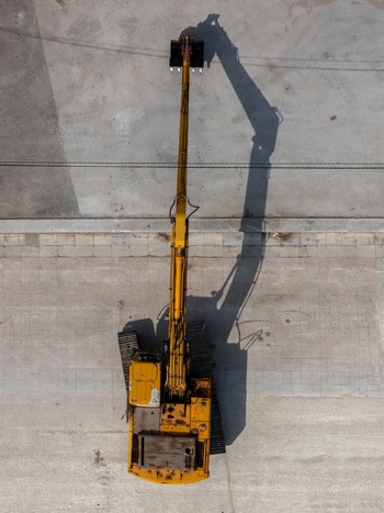 Aerial view of yellow excavator on a paved construction site with long shadow cast on the ground in Alges Lisbon Portugal.