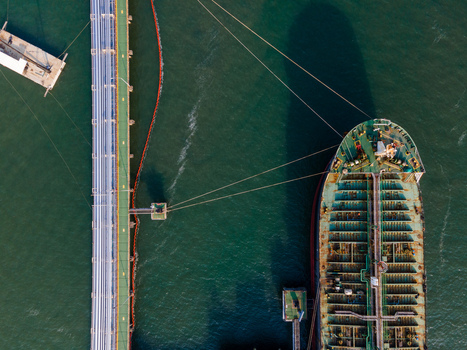 Aerial view of a large oil tanker docked at a long industrial pier in the harbor with calm dark water and mooring lines visible in Cilacap Regency Central Java Indonesia. Aerial view of a large oil tanker docked at a long industrial pier in the harbor with calm dark water and mooring lines visible in Cilacap Regency Central Java Indonesia.