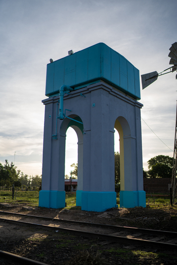 View of the historic water tower with a blue tank atop a grey arched structure situated beside railway tracks in Guaviravi Corrientes Province Argentina.