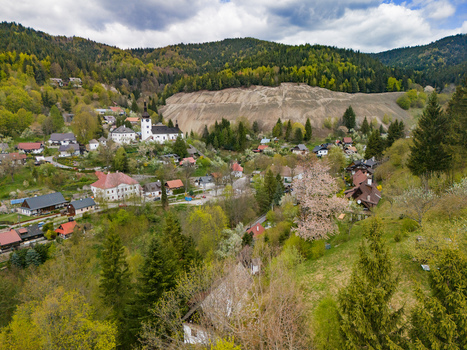 Aerial view of the historic village of Spania Dolina with its white church and traditional houses nestled among green hills and a large mining heap in Spania Dolina Banska Bystrica Region Slovakia.
