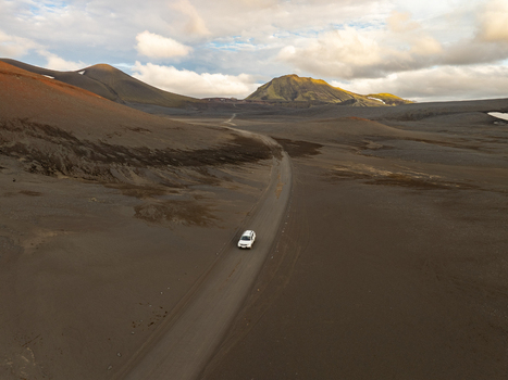 Aerial view of a white car driving on a dirt road through the volcanic landscape of Landmannalaugar in Rangarthing ytra Iceland. Aerial view of a white car driving on a dirt road through the volcanic landscape of Landmannalaugar in Rangarthing ytra Iceland.