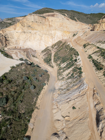 Aerial view of a large open pit quarry with terraced rock faces and dirt access roads surrounded by Mediterranean vegetation in Teulada Valencian Community Spain.