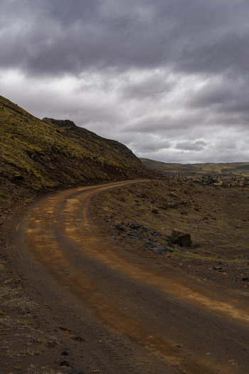 View of a winding dirt road cuts through a rugged mossy landscape under a stormy sky with earthy tones contrasting against the muted greens Skaftárhreppur Iceland. View of a winding dirt road cuts through a rugged mossy landscape under a stormy sky with earthy tones contrasting against the muted greens Skaftárhreppur Iceland.