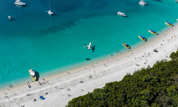 Aerial view of Whitehaven Beach with a seaplane anchored in turquoise water boats along the white sand shore and lush forest in Whitsundays Queensland Australia.