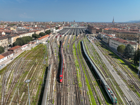 Aerial view of Porta Nuova railway station with a red high speed train on the tracks and the city skyline featuring the Mole Antonelliana in Turin Piedmont Italy. Aerial view of Porta Nuova railway station with a red high speed train on the tracks and the city skyline featuring the Mole Antonelliana in Turin Piedmont Italy.