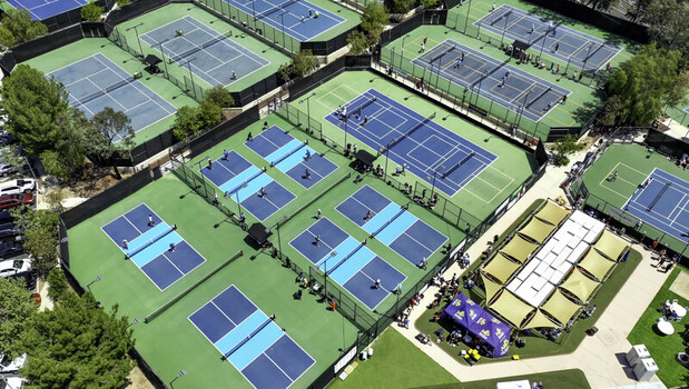 Aerial view of a pickleball tournament with multiple courts featuring players in action on blue and green surfaces with shaded seating areas in Valencia California United States. Aerial view of a pickleball tournament with multiple courts featuring players in action on blue and green surfaces with shaded seating areas in Valencia California United States.