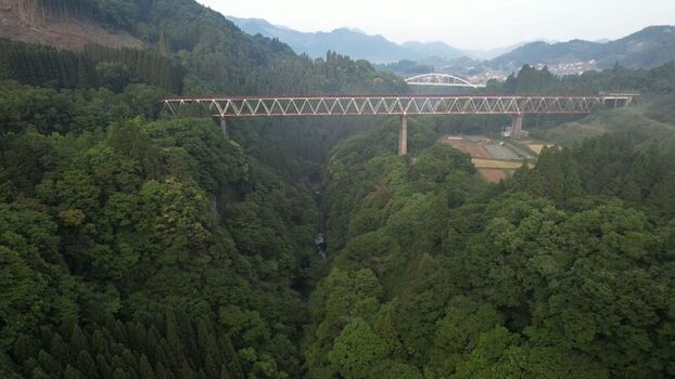 Aerial view of the Amaterasu Railway bridge spanning a deep lush green gorge surrounded by dense forest and mountains in Takachiho Miyazaki Japan.