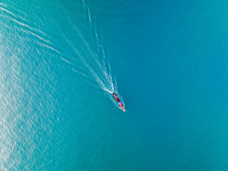 Aerial view of a traditional long tail boat creating a white wake as it travels across the clear turquoise waters of the Gulf of Thailand near Koh Samui Surat Thani Thailand.