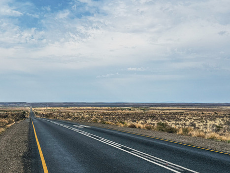 View of a long straight asphalt road stretching through the vast semi arid landscape of the Karoo under a blue sky with scattered clouds in Beaufort West Western Cape South Africa. View of a long straight asphalt road stretching through the vast semi arid landscape of the Karoo under a blue sky with scattered clouds in Beaufort West Western Cape South Africa.