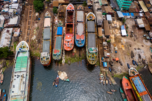 Aerial view of a busy shipyard with multiple cargo ships docked for maintenance and repair surrounded by industrial buildings and urban infrastructure in Dhaka Dhaka Division Bangladesh.