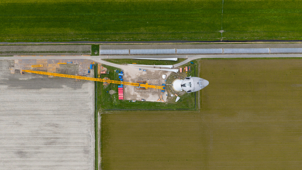 Aerial view of a wind turbine under construction with a large yellow crane and turbine blades on the ground situated amidst agricultural fields in Espel Flevoland Netherlands. Aerial view of a wind turbine under construction with a large yellow crane and turbine blades on the ground situated amidst agricultural fields in Espel Flevoland Netherlands.