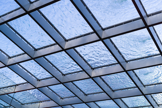 View of a modern glass ceiling with water flowing over the grid structure under a clear blue sky in Bratislava Bratislava Region Slovakia. View of a modern glass ceiling with water flowing over the grid structure under a clear blue sky in Bratislava Bratislava Region Slovakia.