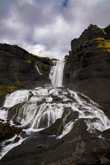 View of cascading waterfall rushes down rugged moss covered cliffs under a dramatic sky creating a stunning display of nature s power Skaftárhreppur Iceland. View of cascading waterfall rushes down rugged moss covered cliffs under a dramatic sky creating a stunning display of nature s power Skaftárhreppur Iceland.
