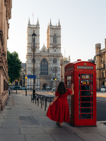 View of a woman in red by an iconic phone booth contrasting with the majestic Westminster Abbey London England United Kingdom. View of a woman in red by an iconic phone booth contrasting with the majestic Westminster Abbey London England United Kingdom.