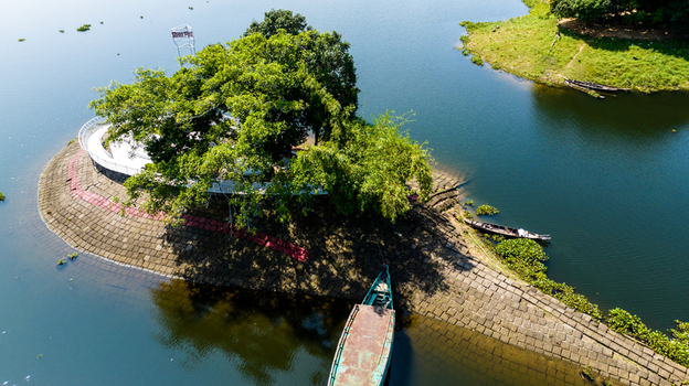 Aerial view of a small island in Kaptai Lake featuring a lush tree a white circular walkway and a wooden boat docked at the stone paved shore in Rangamati Chittagong Division Bangladesh.