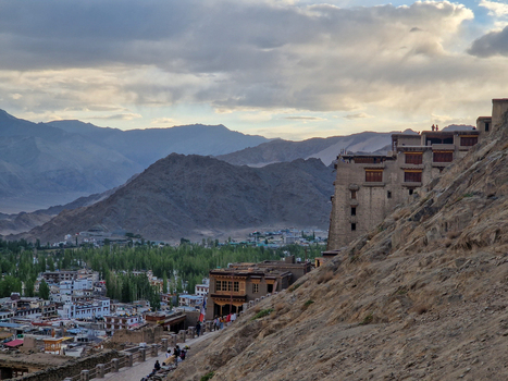 View of Leh Palace perched on a rocky hillside overlooking the town of Leh with distant mountains under a cloudy sky in Leh Ladakh India.