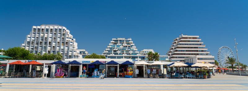 La Grande Motte France 17 July 2026 View of the iconic pyramid shaped apartment buildings along the promenade featuring a ferris wheel in the background under a clear blue sky.