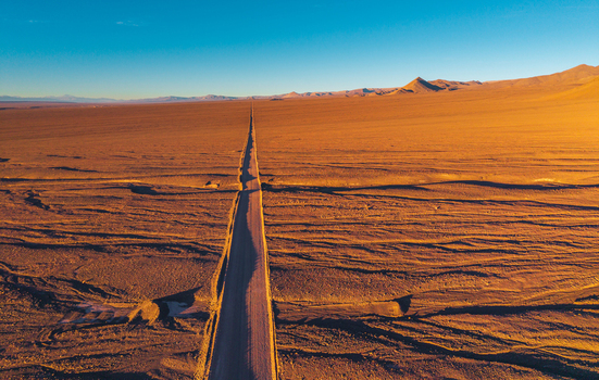 Aerial view of a long straight road cutting through the vast arid desert landscape under a clear blue sky in San Pedro de Atacama Antofagasta Chile. Aerial view of a long straight road cutting through the vast arid desert landscape under a clear blue sky in San Pedro de Atacama Antofagasta Chile.