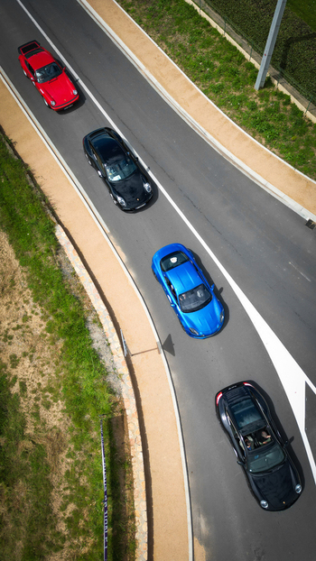 Aerial view of four luxury sports cars driving in a convoy on a paved road surrounded by green grass in La Chapelle de Guinchay Bourgogne Franche Comte France.