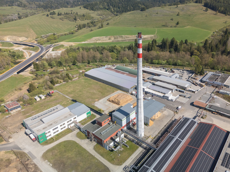 Aerial view of an industrial complex with a tall red and white chimney warehouses and solar panels near a highway bridge and green hills in Nizna Zilina Region Slovakia. Aerial view of an industrial complex with a tall red and white chimney warehouses and solar panels near a highway bridge and green hills in Nizna Zilina Region Slovakia.