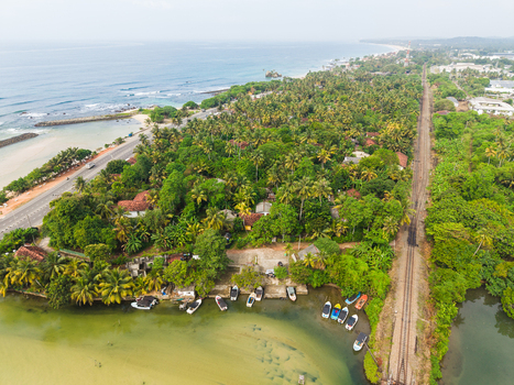 Aerial view of lush tropical vegetation a railway track and small boats moored along the lagoon shore near the ocean Koggala Southern Province Sri Lanka. Aerial view of lush tropical vegetation a railway track and small boats moored along the lagoon shore near the ocean Koggala Southern Province Sri Lanka.