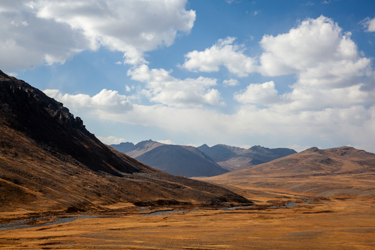 View of the vast golden plains and winding stream of Deosai National Park under a bright blue sky with scattered clouds in Astore Gilgit Pakistan. View of the vast golden plains and winding stream of Deosai National Park under a bright blue sky with scattered clouds in Astore Gilgit Pakistan.