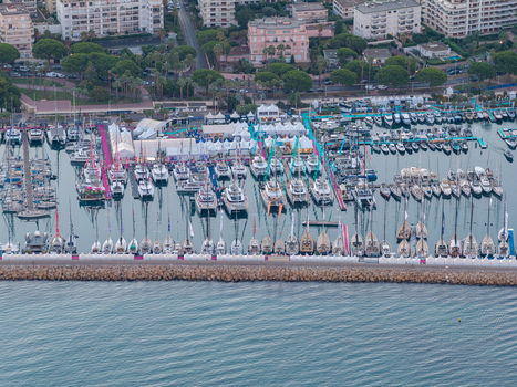 Aerial view of the marina in Cannes filled with numerous yachts and sailboats docked along the pier with white event tents and urban buildings in Cannes Provence Alpes Cote d Azur France. Aerial view of the marina in Cannes filled with numerous yachts and sailboats docked along the pier with white event tents and urban buildings in Cannes Provence Alpes Cote d Azur France.