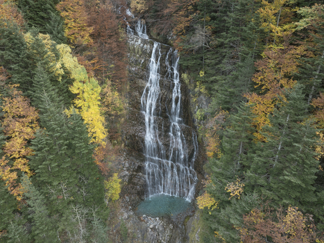 Aerial view of the Pyrenees waterfall cascading down a rocky cliff surrounded by vibrant autumn foliage in the forest in Spain. Aerial view of the Pyrenees waterfall cascading down a rocky cliff surrounded by vibrant autumn foliage in the forest in Spain.