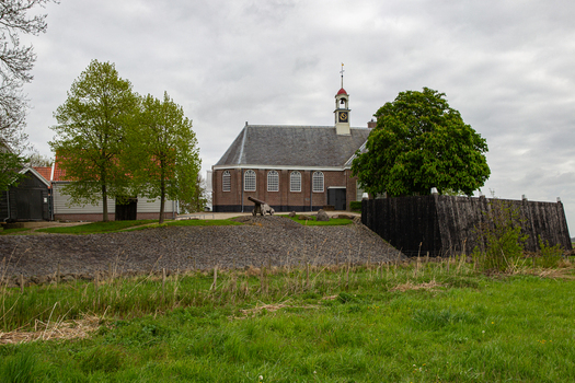View of the historic church and museum buildings at Middelbuurt on the former island of Schokland with lush green trees and a cloudy sky in Schokland Flevoland Netherlands.