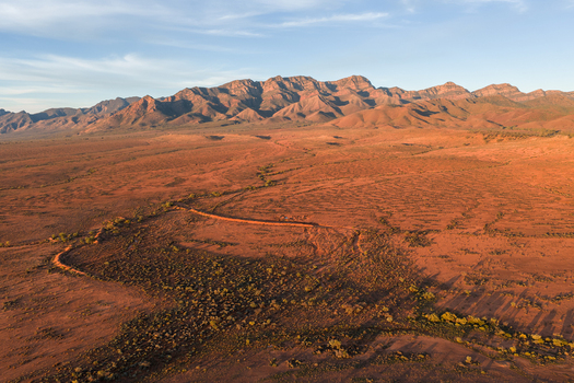 Aerial view of the rugged mountain peaks and red desert landscape of the outback under a soft golden light in Flinders Ranges South Australia Australia. Aerial view of the rugged mountain peaks and red desert landscape of the outback under a soft golden light in Flinders Ranges South Australia Australia.