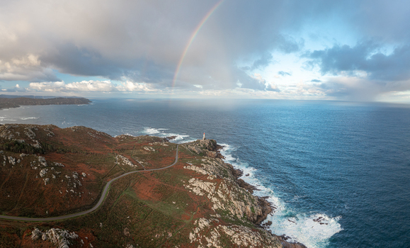 Aerial view of Faro de Punta Nariga lighthouse on rocky cliffs with a winding road and a rainbow over the Atlantic Ocean in Malpica A Coruna Spain. Aerial view of Faro de Punta Nariga lighthouse on rocky cliffs with a winding road and a rainbow over the Atlantic Ocean in Malpica A Coruna Spain.