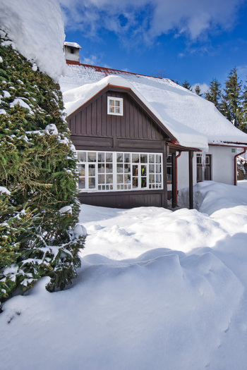 View of a snow covered chalet with dark brown walls and white window frames nestled among snowdrifts under a blue sky Donovaly Banskobystricky kraj Slovakia. View of a snow covered chalet with dark brown walls and white window frames nestled among snowdrifts under a blue sky Donovaly Banskobystricky kraj Slovakia.
