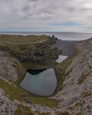 Aerial view of Djupalonssandur featuring black sand beach volcanic rock formations and small pools of water along the rugged coastline of Iceland. Aerial view of Djupalonssandur featuring black sand beach volcanic rock formations and small pools of water along the rugged coastline of Iceland.