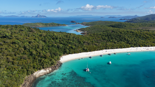 Aerial view of Whitehaven Beach with its iconic white silica sand and turquoise waters surrounded by lush tropical forest and anchored catamarans in Whitsundays Queensland Australia.