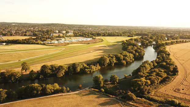 Aerial view of the River Thames winding through lush fields and trees near the racecourse in Windsor England United Kingdom. Aerial view of the River Thames winding through lush fields and trees near the racecourse in Windsor England United Kingdom.