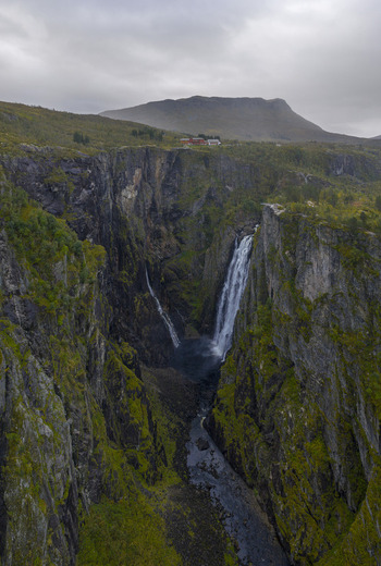 Aerial view of Voringfossen waterfall cascading into a deep rocky canyon with mossy cliffs and buildings on the plateau in Eidfjord Municipality Vestland Norway.