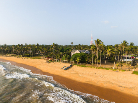Aerial view of a sandy beach with palm trees a traditional boat and a communication tower under a clear sky in Galle Southern Province Sri Lanka.