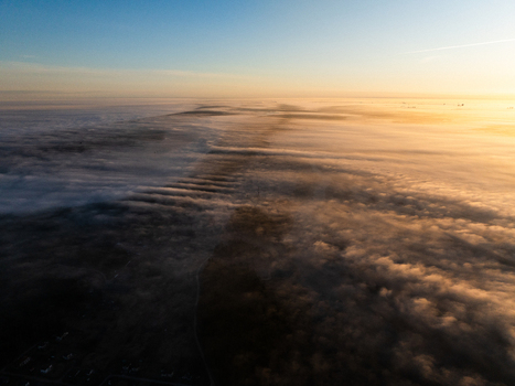 Aerial view of Lake Babite covered in thick morning fog during sunrise with golden light illuminating the clouds Marupes novads Latvia. Aerial view of Lake Babite covered in thick morning fog during sunrise with golden light illuminating the clouds Marupes novads Latvia.