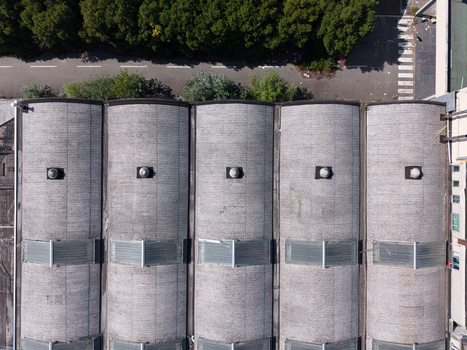 Aerial view of the industrial building featuring arched roof sections with skylights and vents situated next to a road and trees Casale Monferrato Piedmont Italy. Aerial view of the industrial building featuring arched roof sections with skylights and vents situated next to a road and trees Casale Monferrato Piedmont Italy.